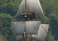 Vintage ship sailing near green shoreline